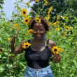 headshot i guess Debbie Long head shot: Black person wearing a tank top and glasses standing among sunflowers